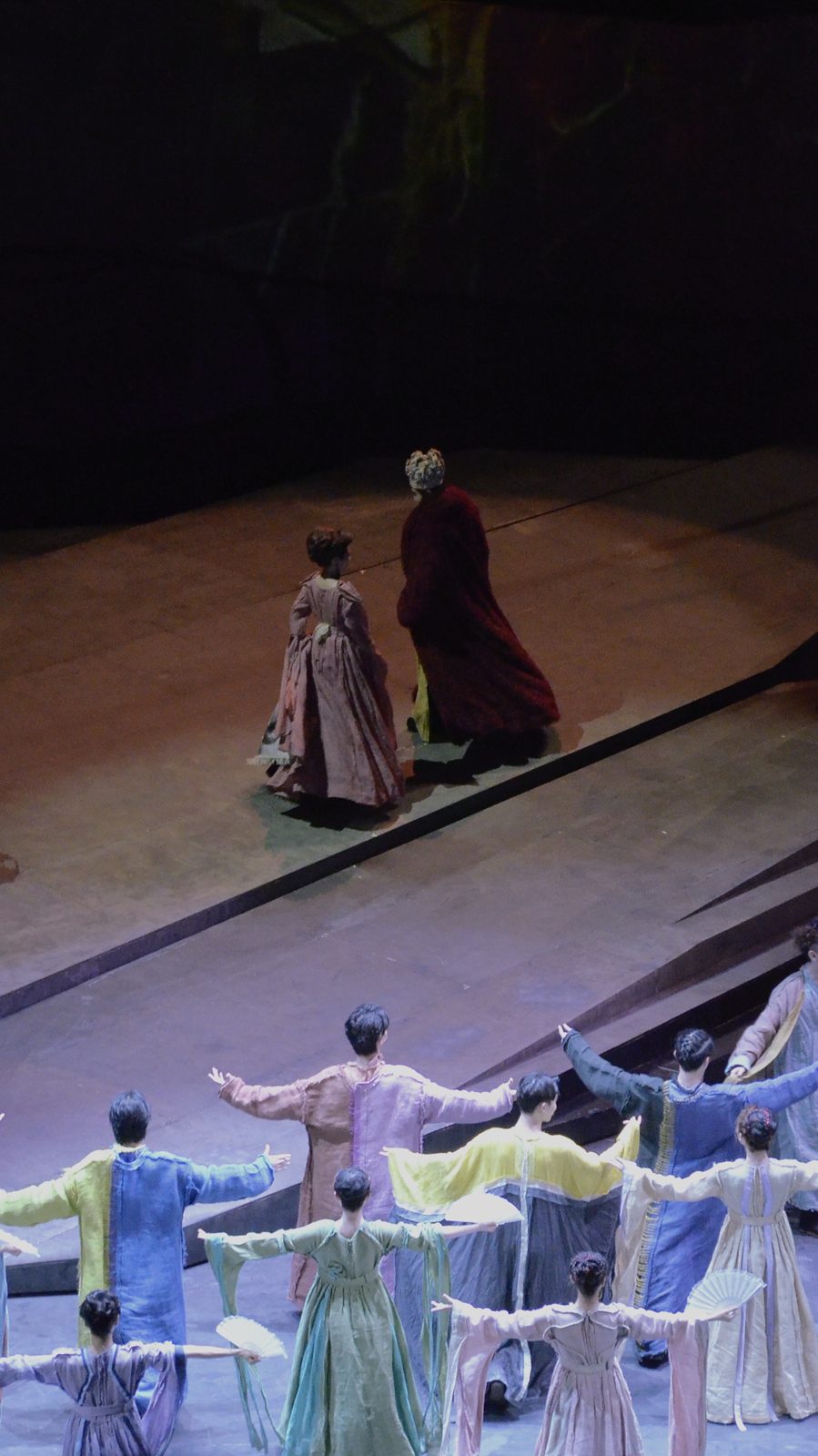 Two actors walk upstage as the ensemble faces them, seen from above
